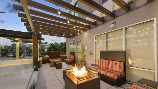 Een terras buiten met een vuurplaats, zitplaatsen en een pergola met lichtjes.
