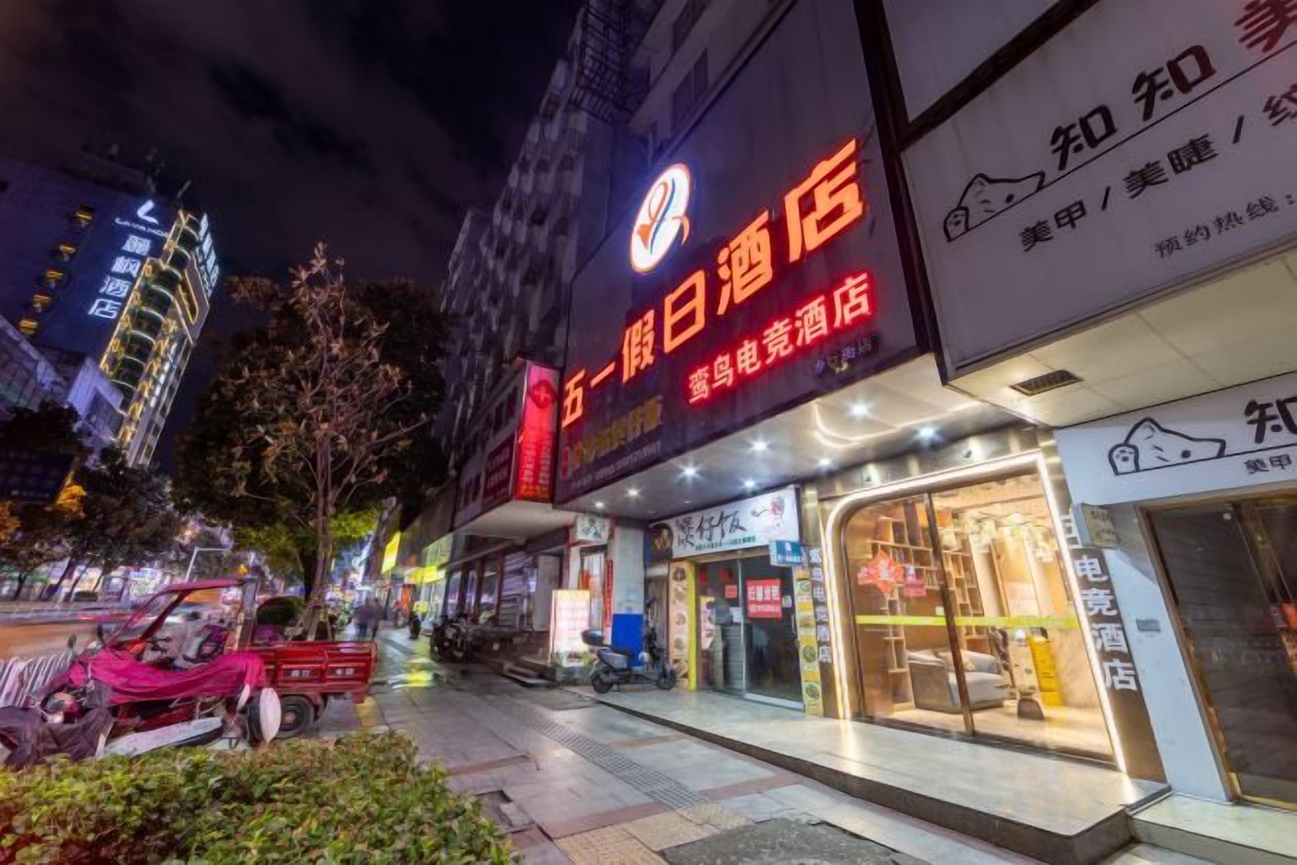 A hotel with illuminated signage, a visible entrance, and a street view with parked vehicles and trees.