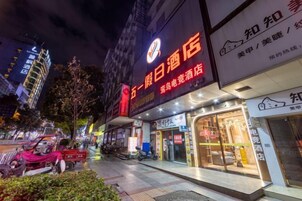 A hotel with illuminated signage, a visible entrance, and a street view with parked vehicles and trees.