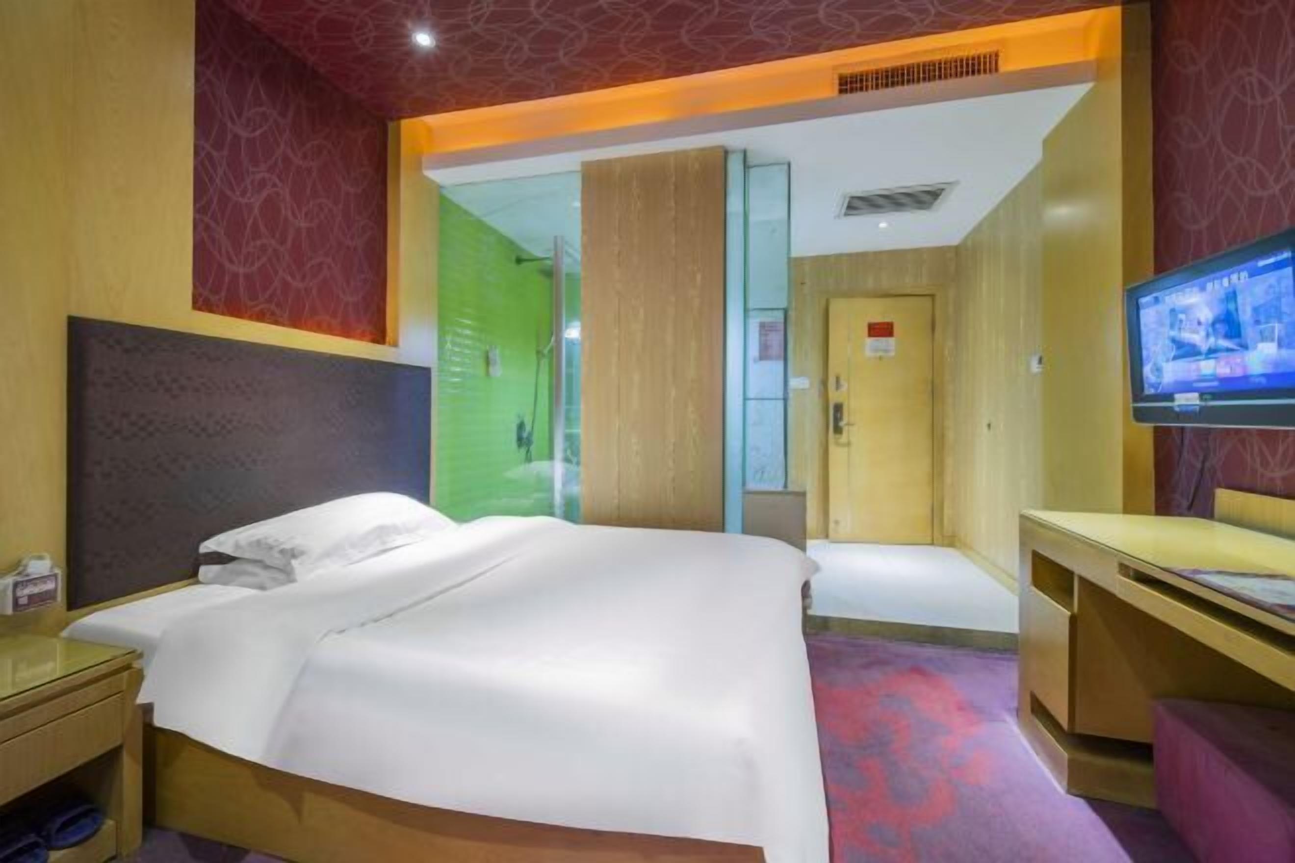 A hotel room with a large bed, a desk, a television, and a door leading to a hallway.