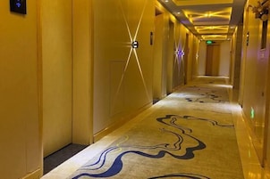 Un pasillo de hotel con alfombra estampada, luminarias fijadas a la pared e iluminación empotrada en el techo.