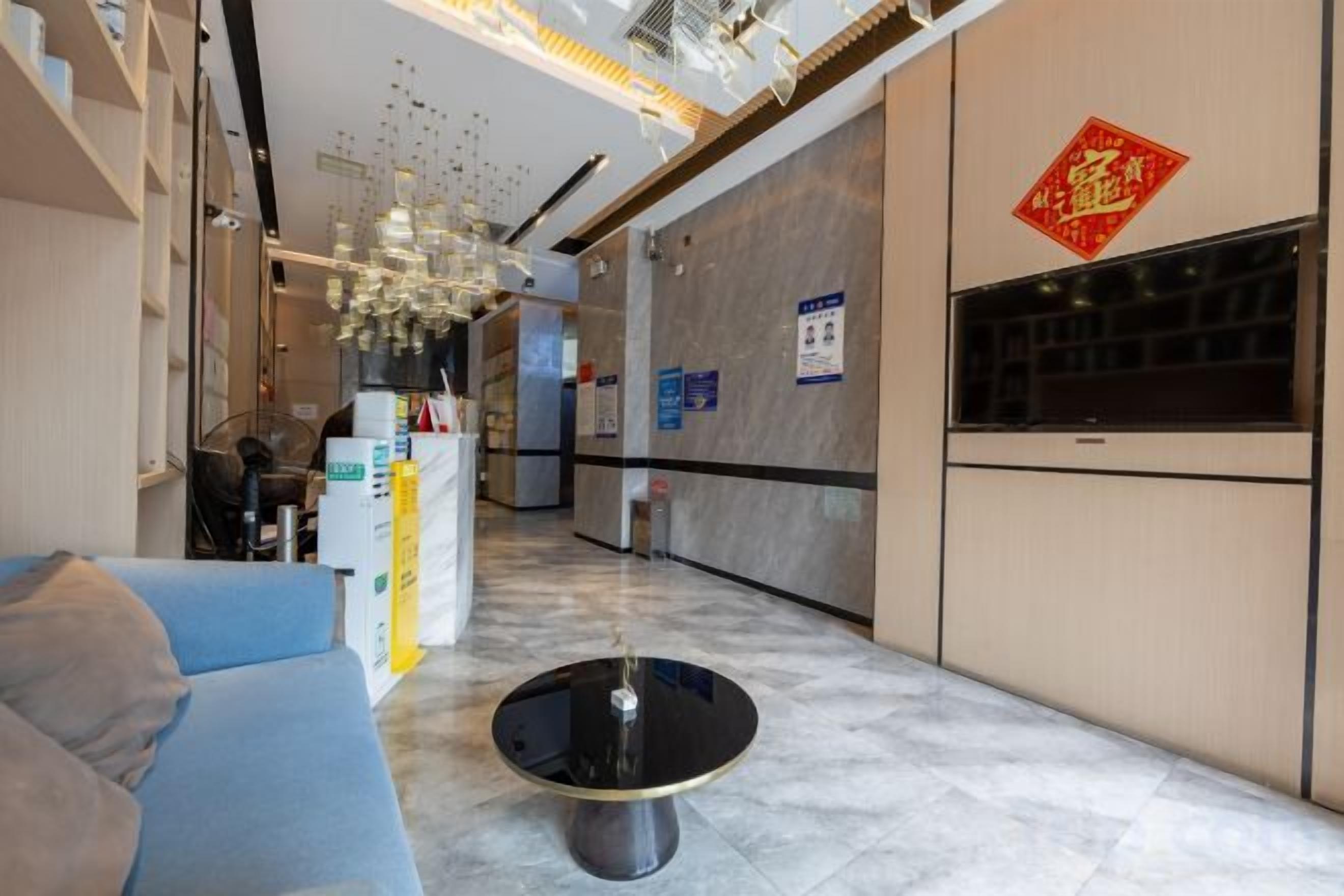 Eine Hotelhalle mit einer Rezeption, einem blauen Sofa, einem schwarzen Couchtisch und einer dekorativen Pendelleuchte.