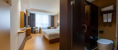A hotel room with a bed, a desk, a chair, a mirror, a window with curtains, a bathroom with a toilet, and a shower area.