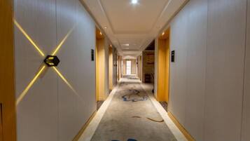 A hotel corridor with a carpeted floor, a light-colored wall with a geometric design, and a door at the end.