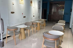 Un espace détente avec des tables et des chaises rondes, un sol carrelé et un mur bleu orné de cadres contenant des certificats.