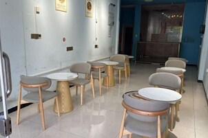 Un área de estar con mesas y sillas redondas, piso de baldosas y una pared azul con diplomas enmarcados.