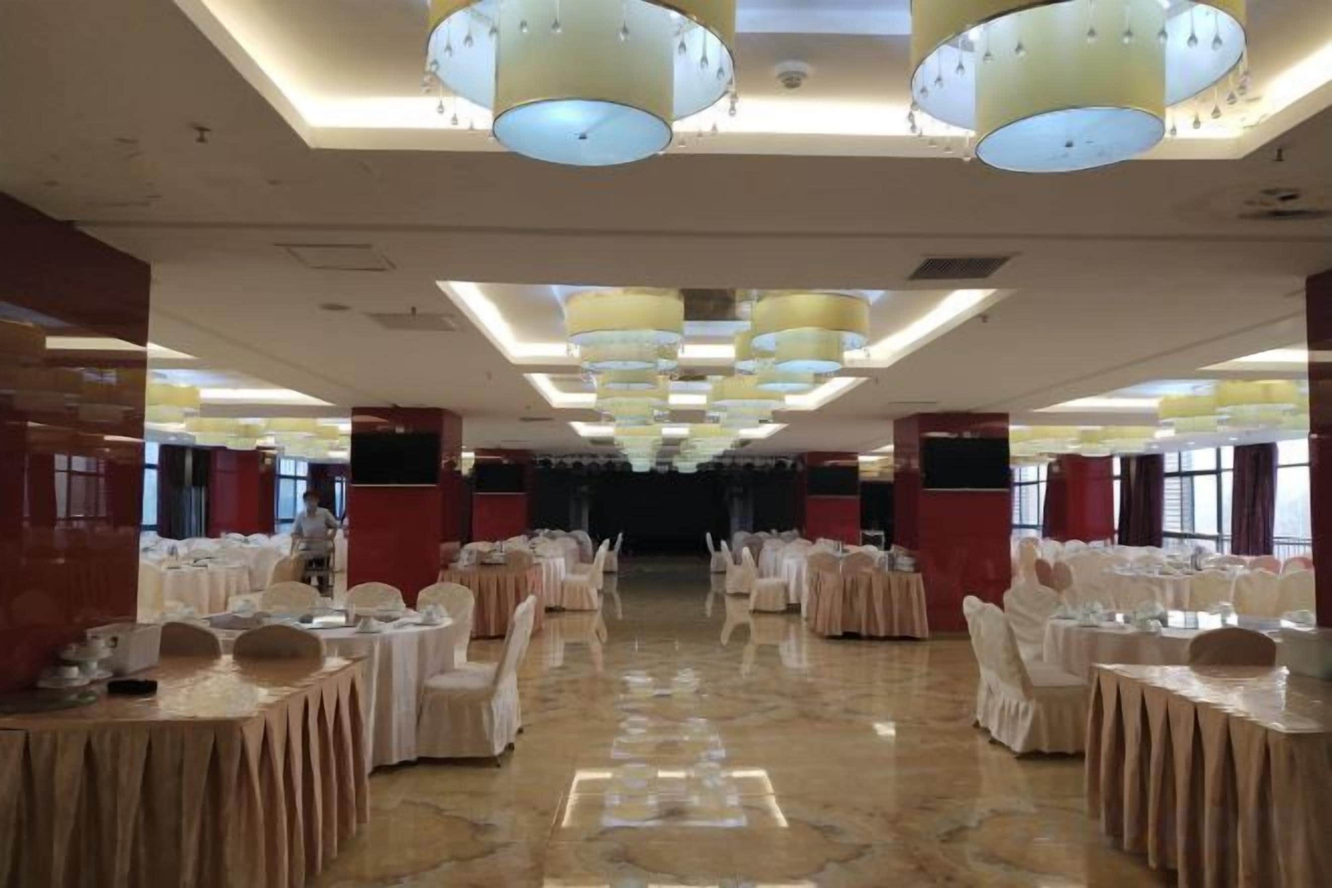 A banquet hall with round tables, chairs, and overhead lighting fixtures.