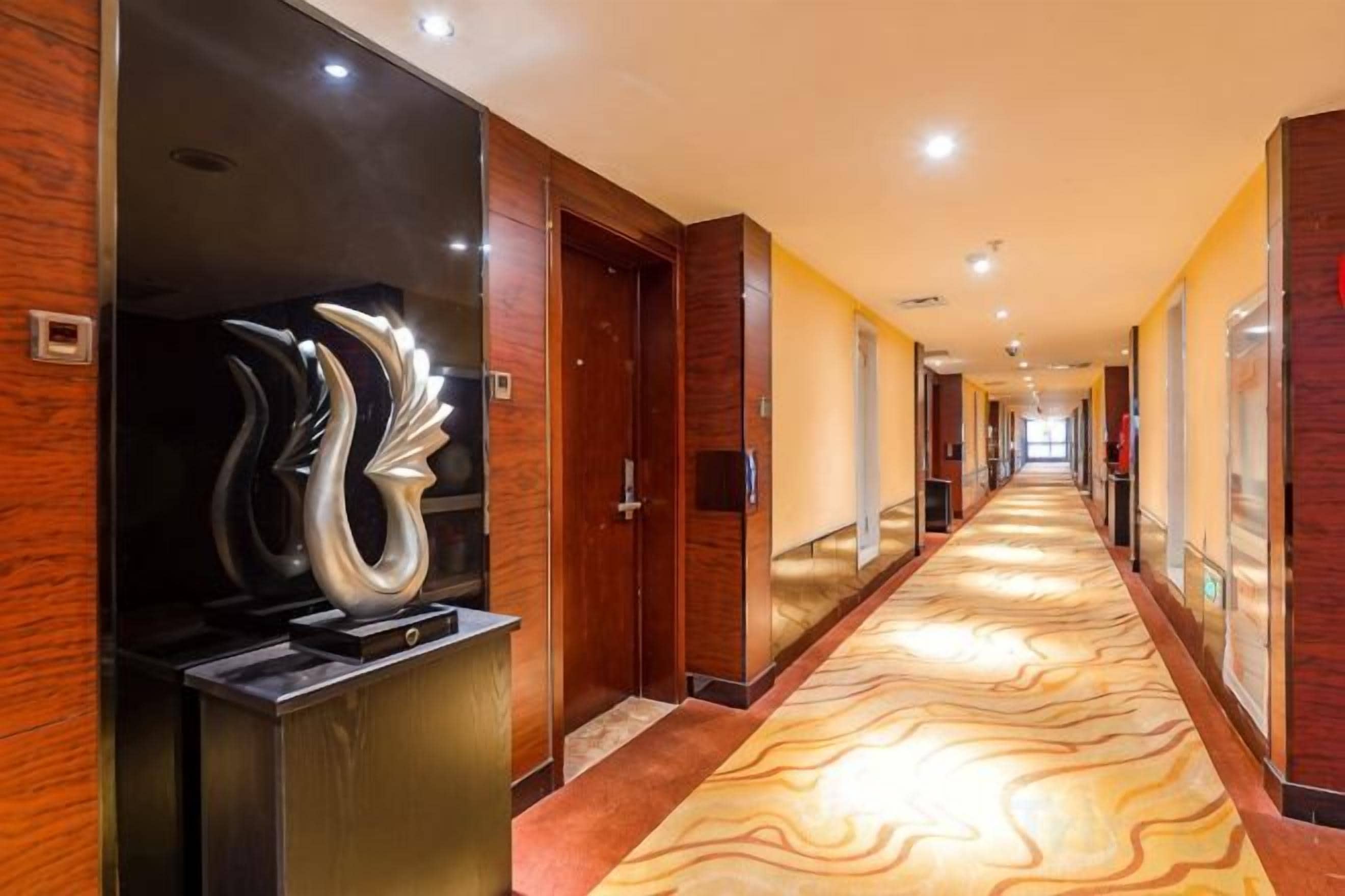 Un pasillo de hotel con alfombra estampada, paredes de madera y una escultura moderna.