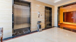 A modern lobby with two elevators, a marble floor, and a wooden door leading to another room. - Longfengxiang Hotel (Dongying)