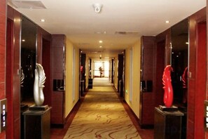 A hotel hallway with a patterned carpet, wooden walls, and two sculptures on pedestals. - Longfengxiang Hotel (Dongying)