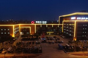 A multi-story hotel with a prominent sign, a parking lot, and a well-lit entrance. - Longfengxiang Hotel (Dongying)