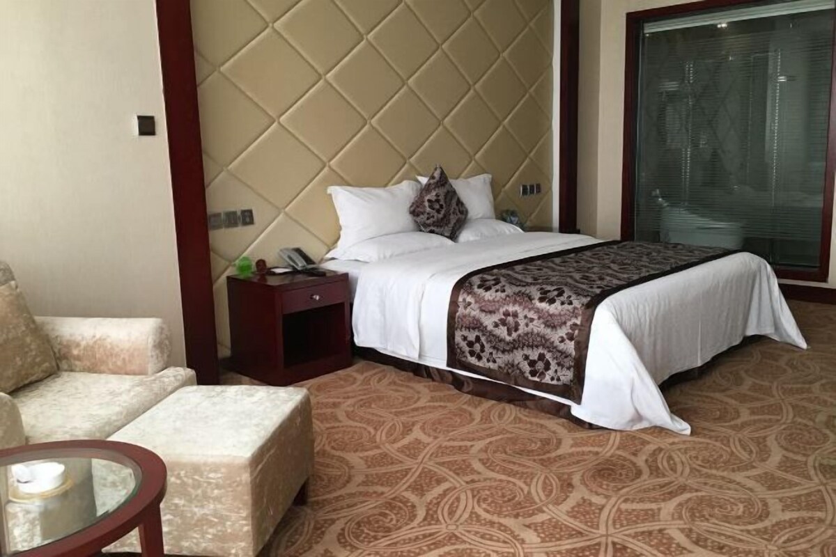 A hotel room with a bed, a nightstand, a chair, and a glass table.