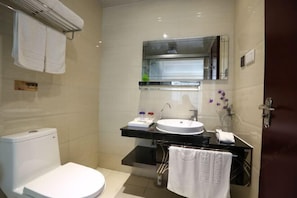 A compact bathroom with a white toilet, a sink with a mirror above it, and a towel rack with towels. - Longfengxiang Hotel (Dongying)
