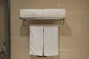 Casa de banho com cabine de duche em vidro, um porta-toalhas com duas toalhas brancas e parede revestida a azulejos.