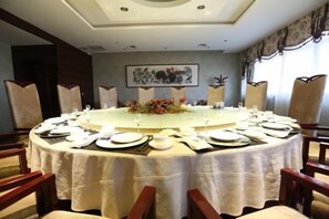 Une table de salle à manger ronde, préparée pour un repas, entourée de chaises, et agrémentée d’un centre de table floral.