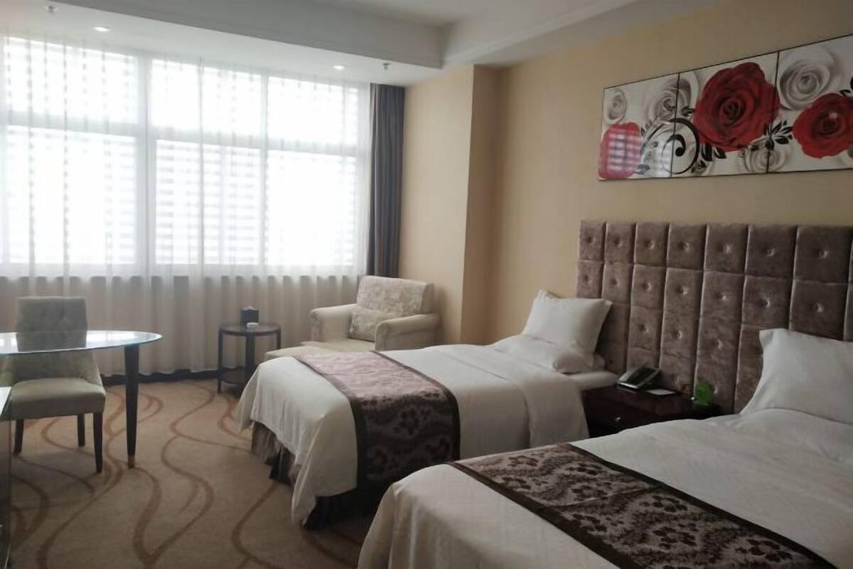 Une chambre d’hôtel avec deux lits, une table à manger ronde, une chaise, une petite table d’appoint et une grande fenêtre avec des rideaux.