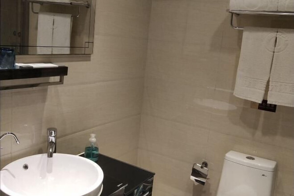 A bathroom with a white sink, mirror, and toilet. There is a shelf with toiletries and a towel rack on the wall.