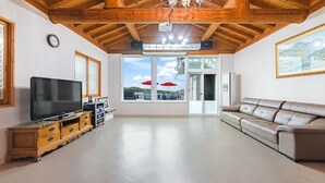 A spacious living room with a television, wooden cabinet, leather sofa, and large windows offering a view of the outdoors. - Daebudo Dekapo Pension (Ansan)