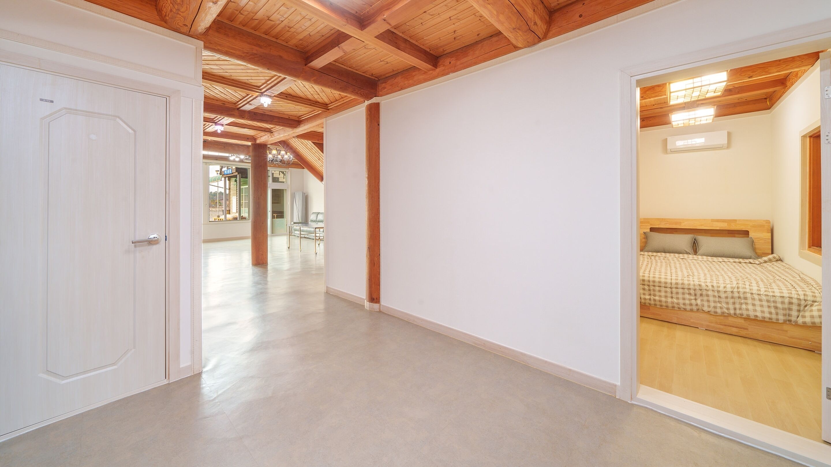 A spacious hallway with a wooden ceiling and a visible bedroom with a bed and a window.