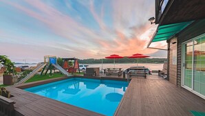 A swimming pool with a slide and play structures, wooden deck, and red umbrellas. - Daebudo Dekapo Pension (Ansan)