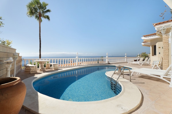 Relax by the serene pool surrounded by a palm tree and tranquil sea views.