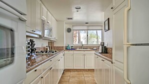 A narrow kitchen with white cabinets, a granite countertop, and a window providing natural light. - Sunny, great views, upstairs villa (Cathedral City)