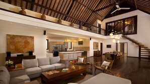 A spacious living area with a high ceiling, a kitchen in the background, and a staircase leading to an upper level. - Villa Tirtadari by Nakula (Kerobokan)