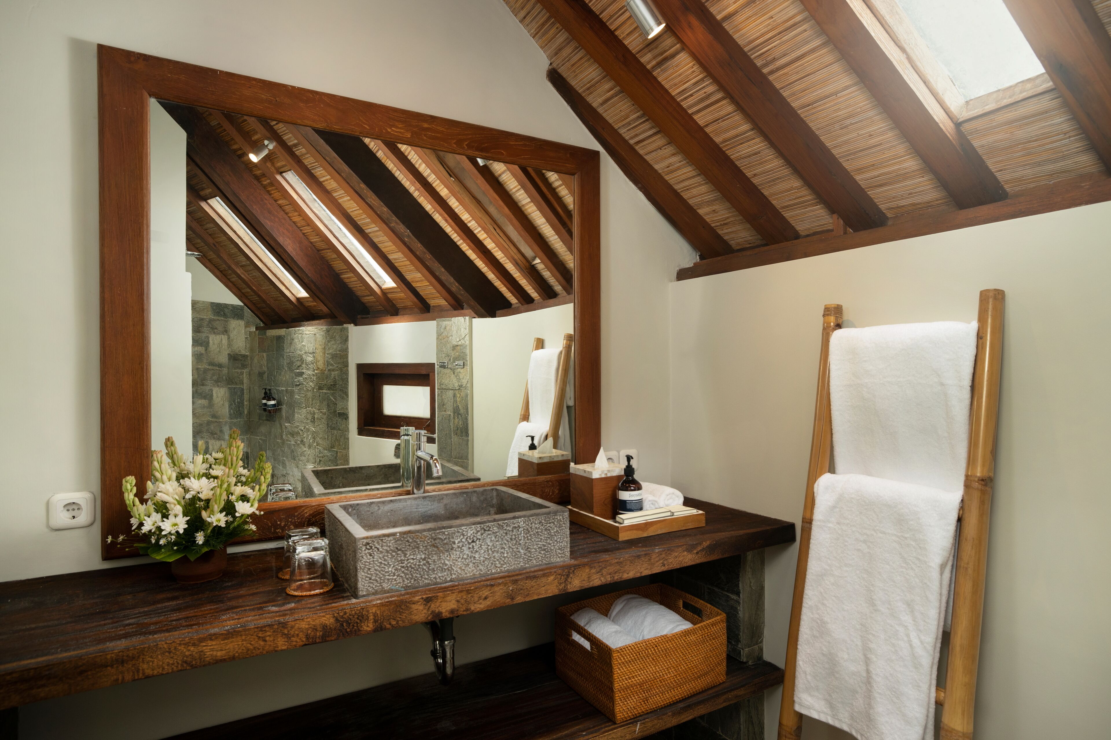 A bathroom with a wooden vanity, a large mirror, a stone sink, a towel rack, and a skylight.