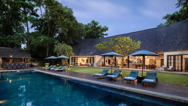 A swimming pool with lounge chairs and umbrellas, surrounded by a building with a covered patio and outdoor seating. - Villa Tirtadari by Nakula (Kerobokan)