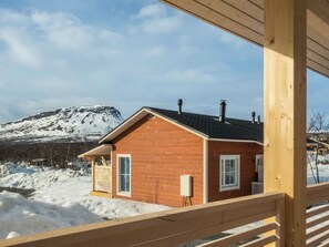 A wooden cabin with a sloped roof, a small porch, and a view of a snow-covered mountain.