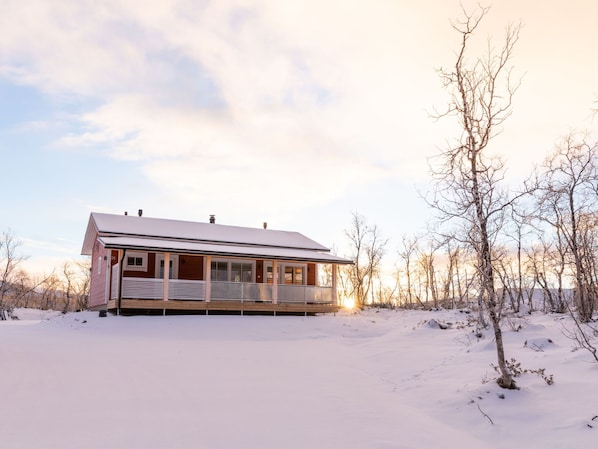 A single-story house with a porch, surrounded by snow-covered ground and trees.