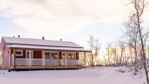 A single-story cabin with a covered porch, surrounded by snow-covered ground and leafless trees. - Saana 3 by Interhome (Enontekiö)