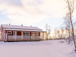 Ett envåningshus med en inglasad veranda, omgivet av snötäckt mark och träd utan löv.