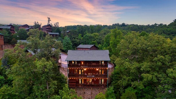 Un chalet à étages doté d’une façade en pierre, entouré d’une forêt dense.