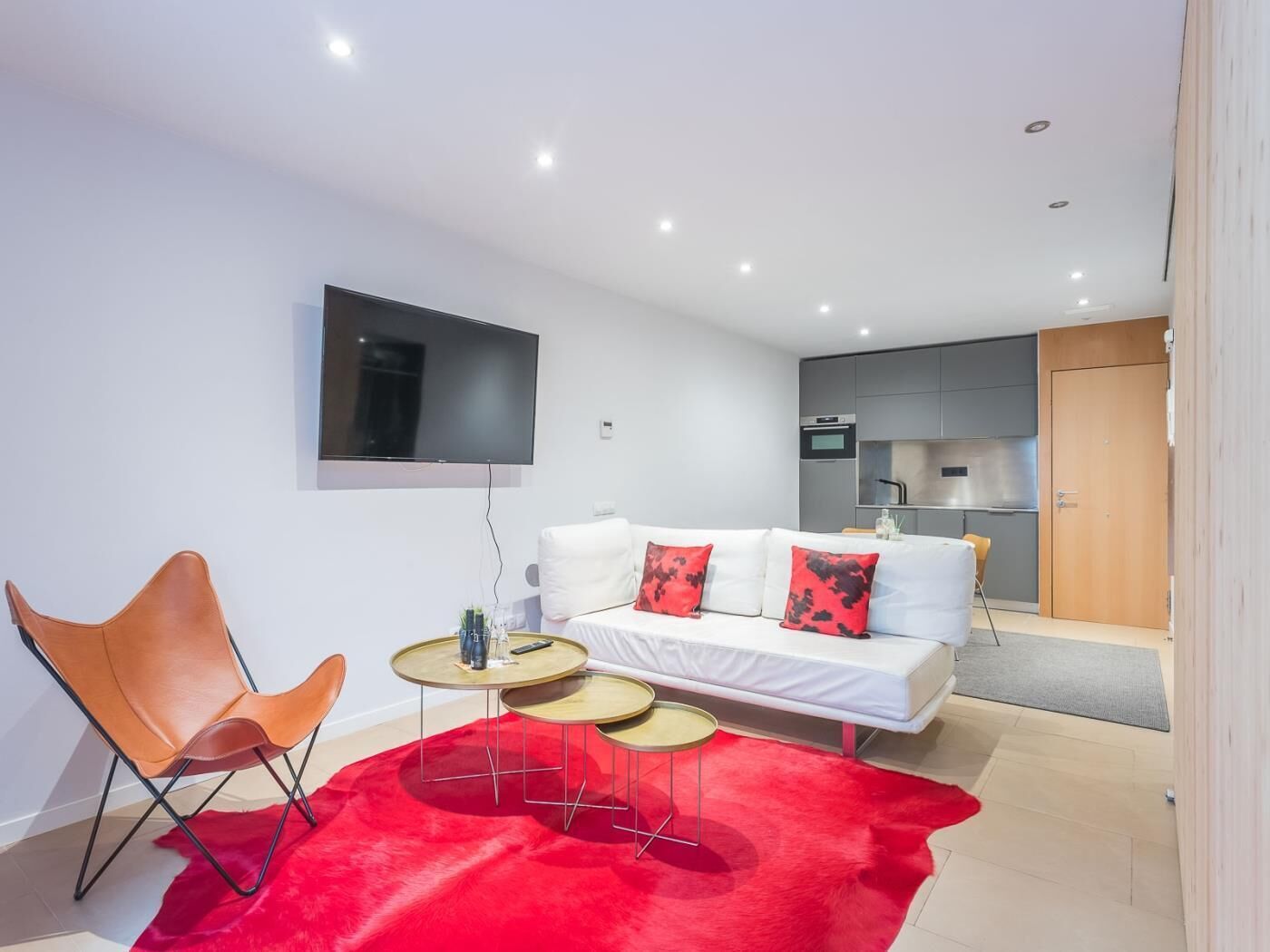 A modern living room with a sofa, a red rug, a TV, and a kitchen in the background.