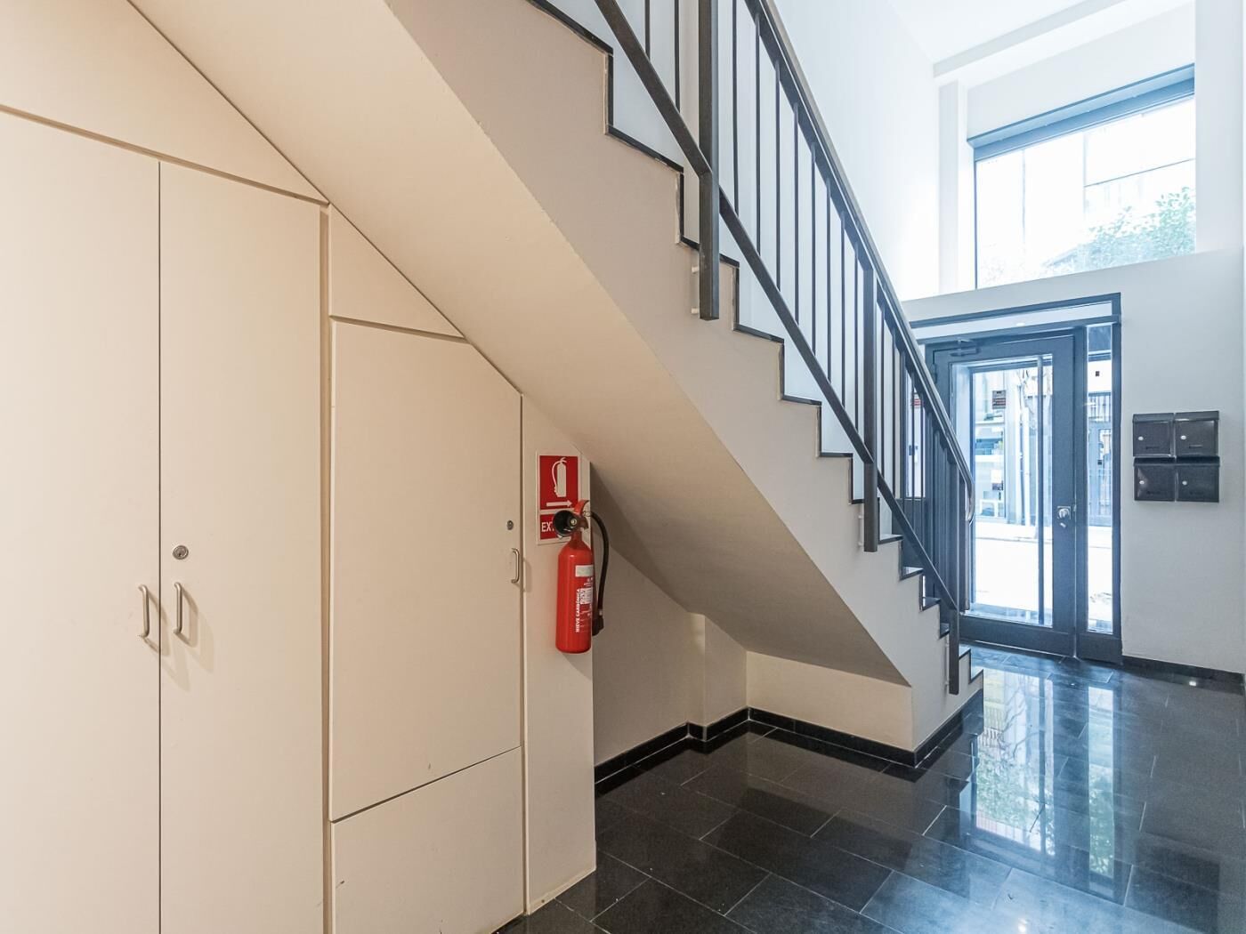 A modern interior with a staircase, a fire extinguisher, and a door with a mailbox.