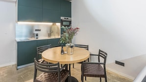 Une cuisine compacte équipée d’un four encastré, d’un évier et d’un petit plan de travail. On y trouve une table ronde en bois, entourée de quatre chaises, et un vase avec des fleurs posé sur la table.