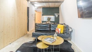 Un salon moderne avec un canapé en cuir noir, deux petites tables rondes et un téléviseur à écran plat fixé au mur.