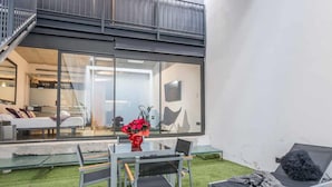 Un espace de vie extérieur moderne doté d’un mur en verre, d’une table à manger, de chaises et d’un fauteuil de détente.