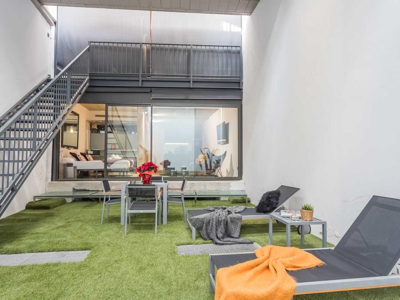 A modern outdoor living area with artificial grass, a lounge chair, a small table, and a staircase leading to an interior space.