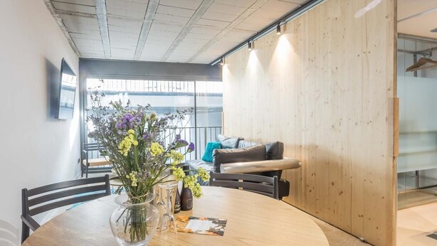 Ett modernt mötesrum med ett runt bord, stolar, en vas med blommor och en soffa i bakgrunden.