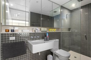 A modern bathroom with a white sink, mirror, and toilet. There are toiletries on the sink and a towel rack. - ✔Sophisticated Designer Condo W River & City Views (Southbank)