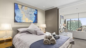 Une chambre d’hôtel moderne, dotée d’un grand lit, de deux tables de chevet, d’un bureau et offrant une vue sur le paysage urbain.