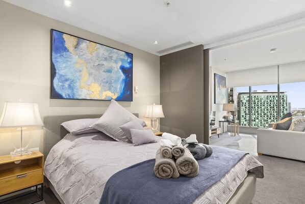 A modern hotel room with a large bed, two bedside tables, a desk, and a view of a cityscape. - ✔Sophisticated Designer Condo W River & City Views (Southbank)