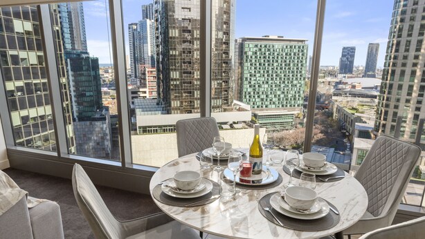 Un coin repas avec une table dressée pour quatre personnes, de grandes fenêtres offrant une vue sur la ville et un mobilier moderne.