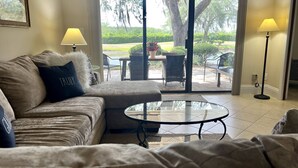 A living room with a sofa, a glass coffee table, and a view of a patio with outdoor furniture.
