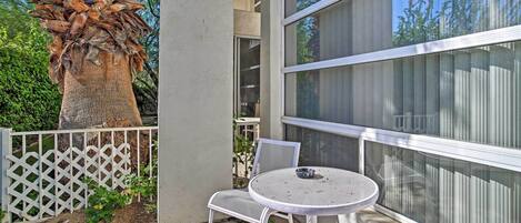 A patio with a white metal table and chairs, a white lattice fence, and a large tree.