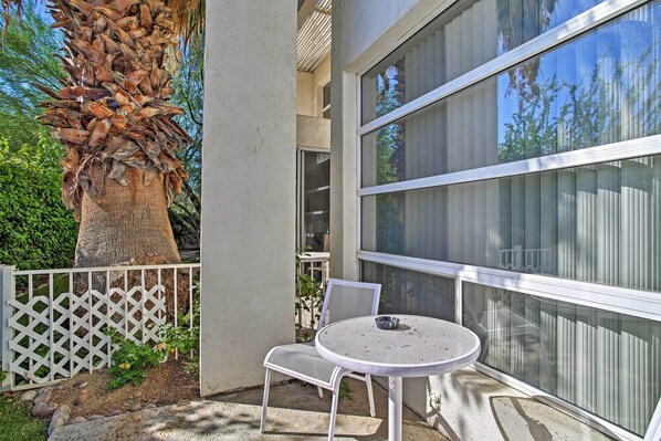 Eine Terrasse mit einem weißen Metalltisch und -stühlen, einem weißen Gitterzaun und einem großen Baum.