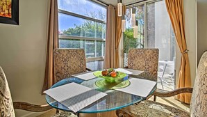 Comedor con mesa de vidrio, sillas estampadas y vista a plantas al exterior.