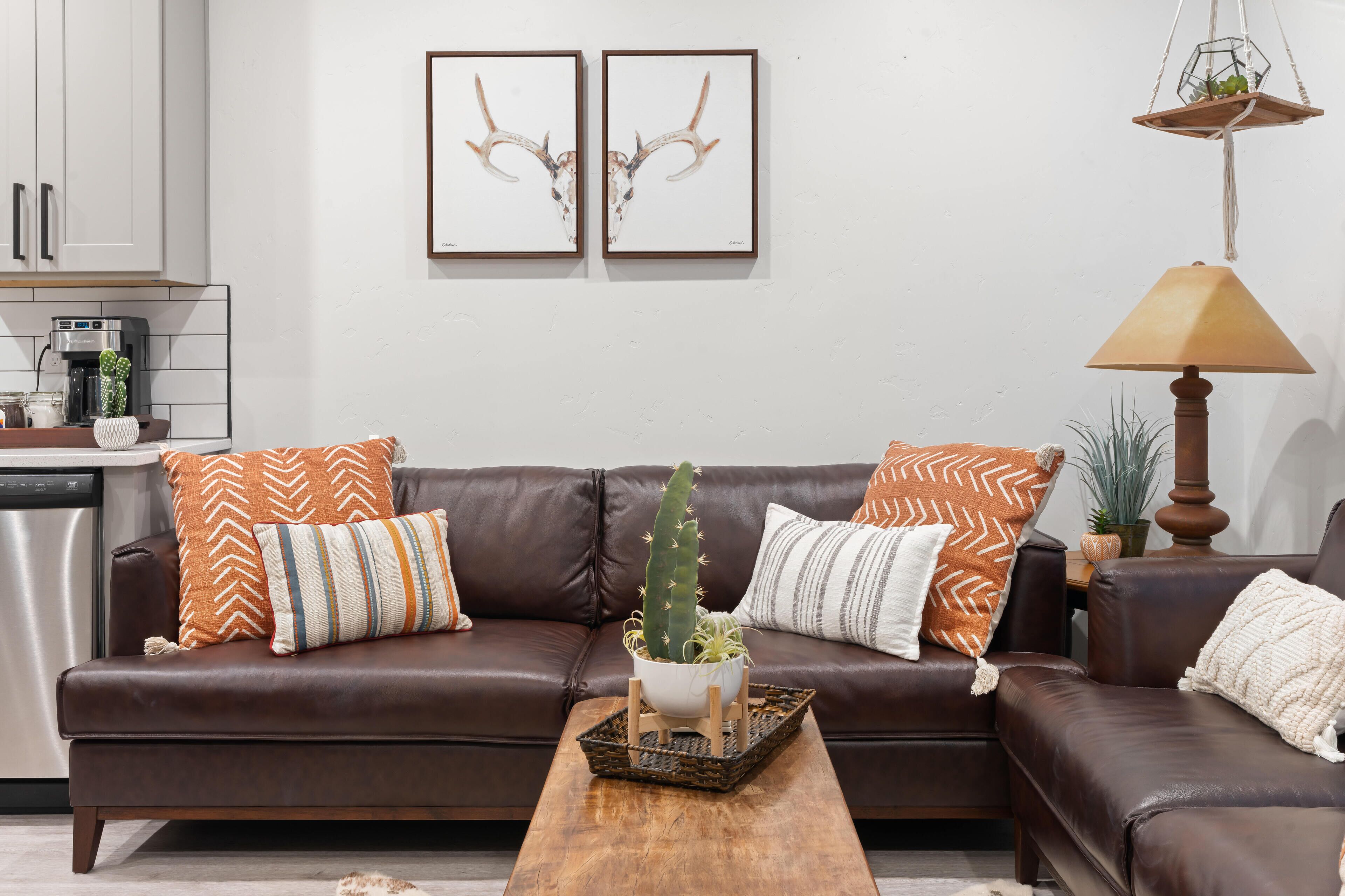 Uma sala de estar moderna com um sofá de couro marrom, dois chifres de veado emoldurados na parede, uma planta cacto no sofá e uma mesa de centro de madeira.